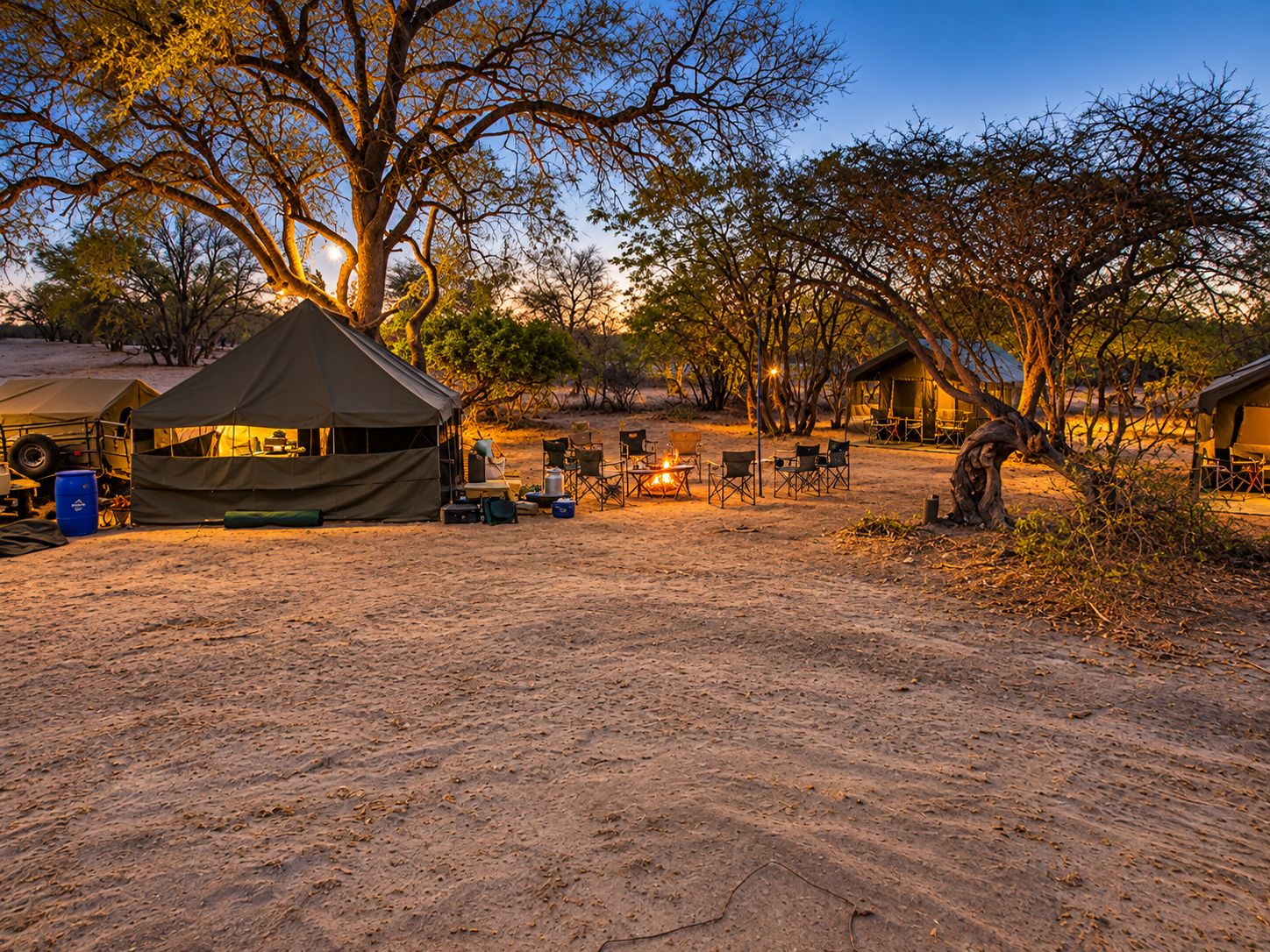 Canvas safari tent lit up at dusk, camp fire burning