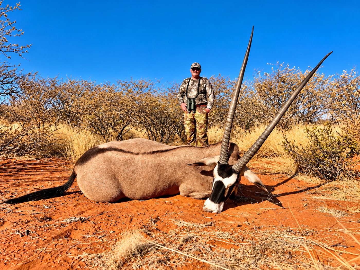 Hunter with a gemsbok on red sand